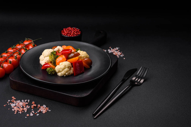 Delicious salad of fresh cherry tomatoes, sweet peppers, broccoli and cauliflower with salt and spices on a dark concrete background - Fotografie, Obrázek
