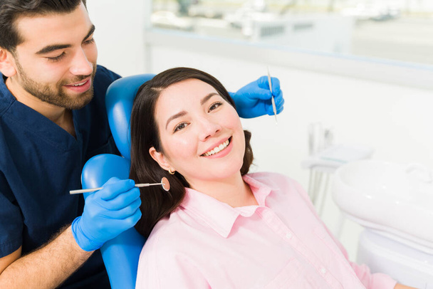Χαρούμενη νεαρή γυναίκα που χαμογελάει στον οδοντίατρο για οδοντιατρική εξέταση ή για να καθαρίσει τα δόντια του.  - Φωτογραφία, εικόνα
