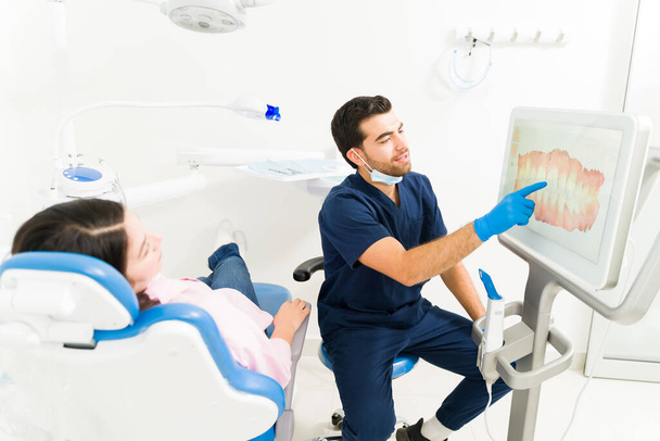 Professioneller Lateinamerikaner und Zahnarzt zeigt einer Patientin, die mit Kieferorthopädie ein neues Lächeln entwerfen will, die 3D-Modelltechnologie - Foto, Bild