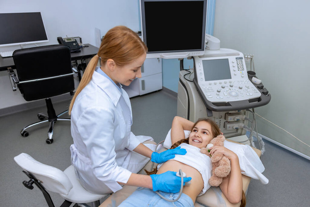 Doctor performing ultrasound scan on school aged girl medical specialist examining child abdominal cavity with sonogram equipment in clinic office. - Фото, зображення
