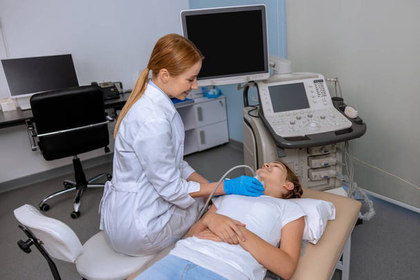 Female doctor performing thyroid ultrasound scan on school aged girl medical specialist examining child neck with sonogram equipment in hospital. - Фото, зображення