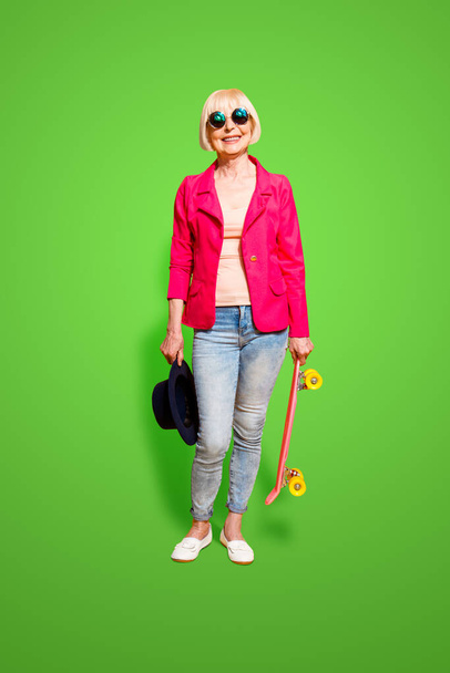 Повноцінний вертикальний портрет сучасної літньої жінки з дошкою для катання на ковзанах ізольовано на жовтому тлі
. - Фото, зображення