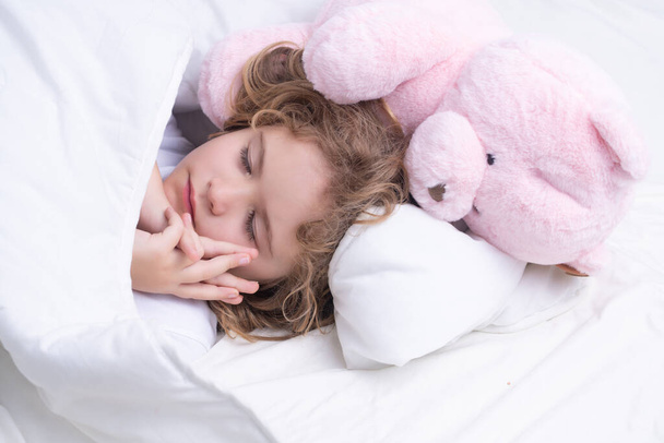Kid sleeping with a toy teddy bear in bed on day. Child sleep, napping. Cute kid sleeping in bed. Sleeping kid face - Фото, изображение