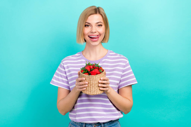 Photo of satisfied woman bob hairdo dressed striped t-shirt hold basket of strawberries tongue lick lips isolated on teal color background. - Fotoğraf, Görsel