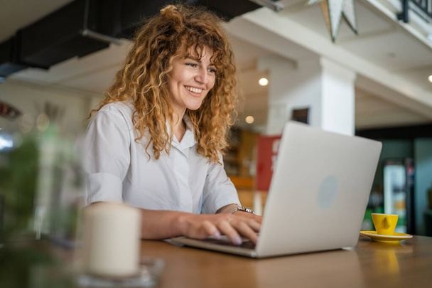 One woman adult caucasian female with curly hair work on laptop computer while sit at cafe real person copy space happy smile confident - Fotografie, Obrázek