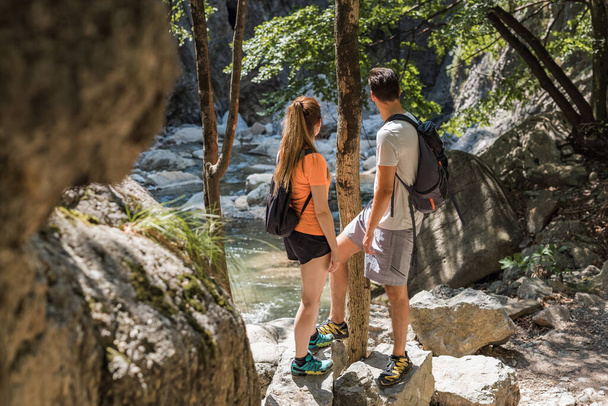 Two tourists, a young couple, enjoying time in nature and hiking, walking along the rocky mountain stream bed and looking in the distance - Photo, Image