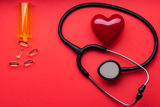 medical stethoscope, red heart and pills on a red background. View from above. Space for text - Photo, image