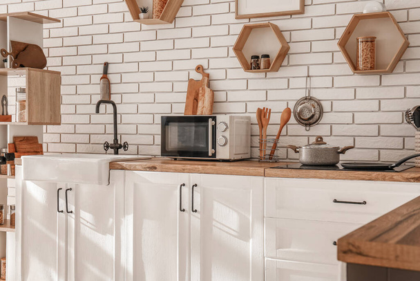 Interior da cozinha moderna com pia, forno de microondas e panela de cozinhar em balcões brancos - Foto, Imagem