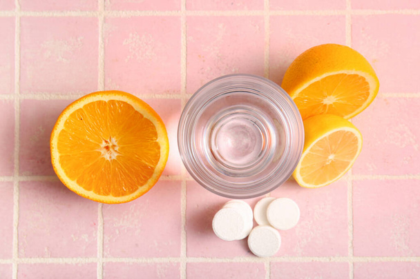 Lasi vettä, C-vitamiini poretabletteja ja hedelmiä vaaleanpunainen kaakeloitu pöytä - Valokuva, kuva