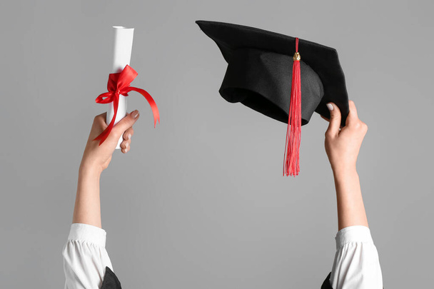 Vrouw met graduatiehoed en diploma op grijze achtergrond - Foto, afbeelding