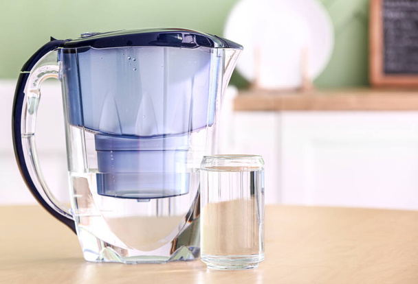 Modern filter jug and glass of water on wooden table in kitchen - Photo, Image