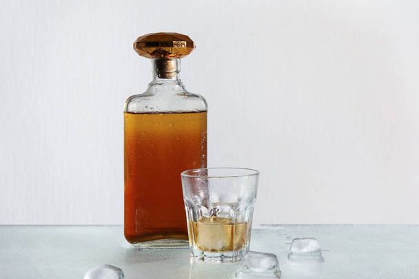 Bottiglia e bicchiere di rum con cubetti di ghiaccio su fondo grigio - Foto, immagini