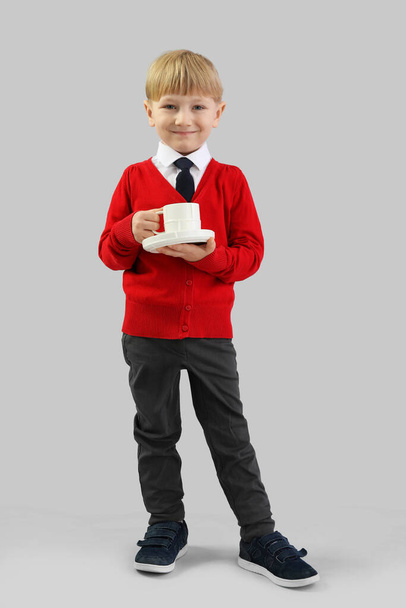 Funny little businessman with cup of coffee on grey background - 写真・画像
