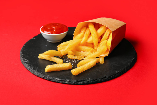Palatábla papírdobozban ízletes sült krumpli és ketchup piros alapon - Fotó, kép