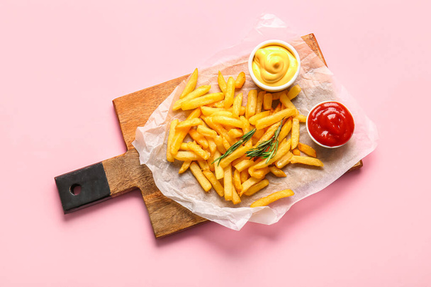 Houten bord met lekkere frietjes, rozemarijn en sauzen op roze achtergrond - Foto, afbeelding