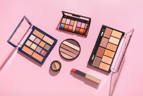 Different palettes of eyeshadows and lipstick on pink background - Zdjęcie, obraz