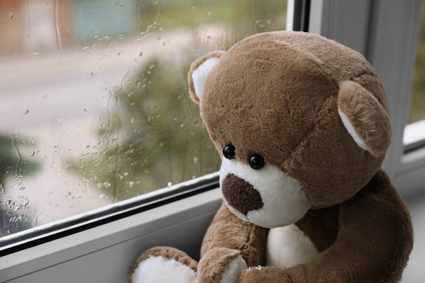 Cute lonely teddy bear on windowsill indoors, closeup. Space for text - Foto, afbeelding