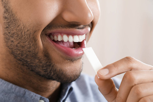 Man with chewing gum on blurred background, closeup - Zdjęcie, obraz