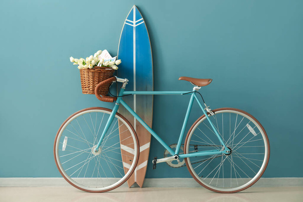 Bicycle with flowers and surfboard near blue wall in room - Photo, Image