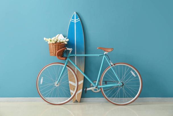 Bicicleta con flores y tabla de surf cerca de la pared azul en la habitación - Foto, Imagen