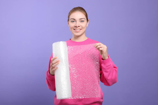 Woman holding roll of bubble wrap on purple background. Stress relief - Photo, image