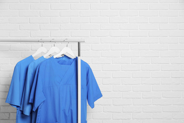 Medical uniforms hanging on rack near white brick wall. Space for text - Foto, afbeelding