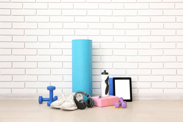 Sports equipment with headphones, tablet computer and bottle near white brick wall - Fotoğraf, Görsel