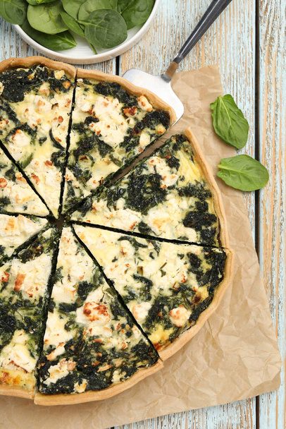 Delicious homemade quiche and fresh spinach leaves on table, flat lay - Fotoğraf, Görsel