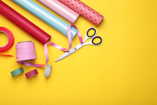 Rolls of colorful wrapping papers, scissors and ribbons on yellow background, flat lay. Space for text - Foto, Imagem
