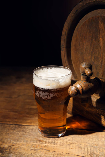 Barril de madera y vaso de cerveza fría sobre mesa sobre fondo oscuro - Foto, imagen