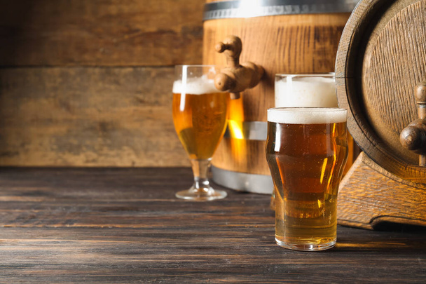 Oak barrels and glasses of cold beer on wooden background - Photo, image