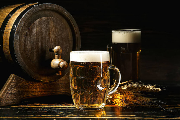 Κούπα κρύας μπύρας και ξύλινη κάννη σε σκούρο φόντο - Φωτογραφία, εικόνα