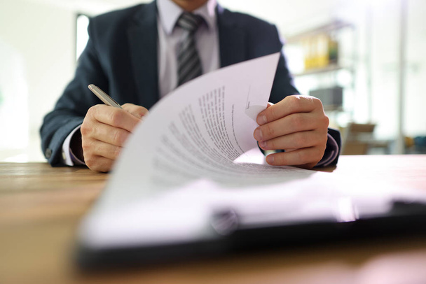 Бизнесмен переворачивает страницу подписания контракта с ручкой после прочтения. Человек в классическом костюме ставит подпись на бумажном листе, делая успешную сделку - Фото, изображение