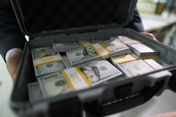 Manager holds open case with counted stacks of dollar banknotes in hands. Man shows briefcase with money paid for successful deal by client - Фото, зображення