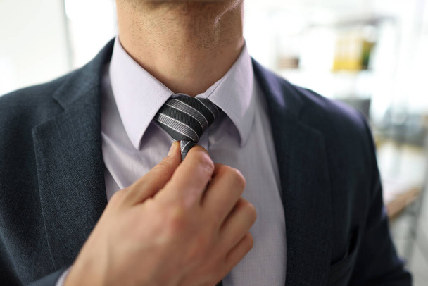Successful businessman adjusts tie in office. Young male office worker maintains solid appearance at workplace on blurred background - Foto, Bild