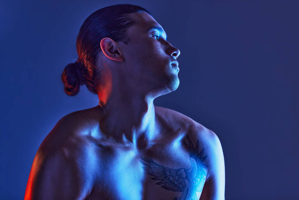 Man, sexy body and light in studio for art, fitness or beauty of a person on a blue background. Face, strong chest and fitness model with a tattoo, glow and creative motivation for aesthetic backdrop. - Foto, Imagem