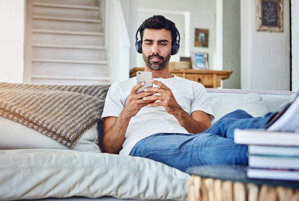 This is how he does days off. a man relaxing on the sofa while using his phone and headphones - Foto, Bild