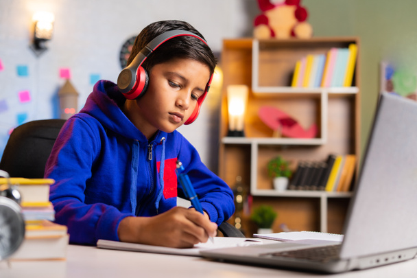 インドの子供は自宅で緑の画面のラップトップ上のオンラインクラスからノートを作る- eラーニング、知性と教育の概念. - 写真・画像
