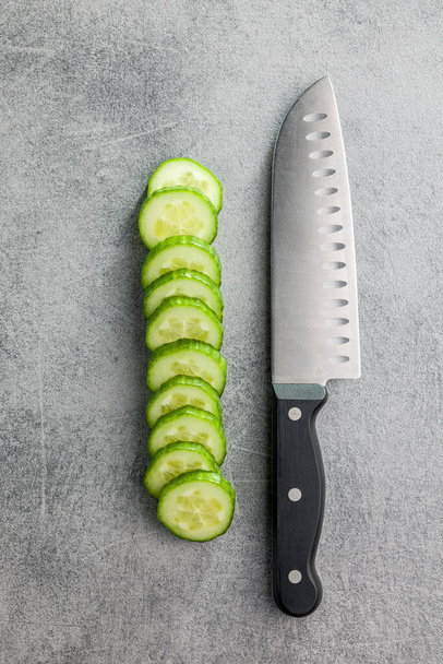 Sliced fresh green cucumber and knife on the kitchen table. Top view. - Foto, imagen