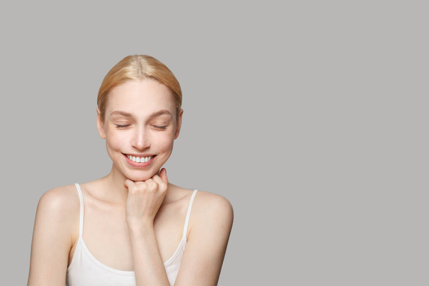 Fröhliches, fröhliches Model mit süßem Lächeln. Gesunde Frau mit frischer Haut posiert mit geschlossenen Augen. Gesichtsbehandlung, Hautpflege und Kosmetologie-Konzept - Foto, Bild