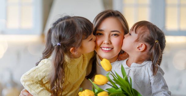 Happy mother's day. Children daughters congratulating mother and giving her bouquet of flowers. - Photo, image