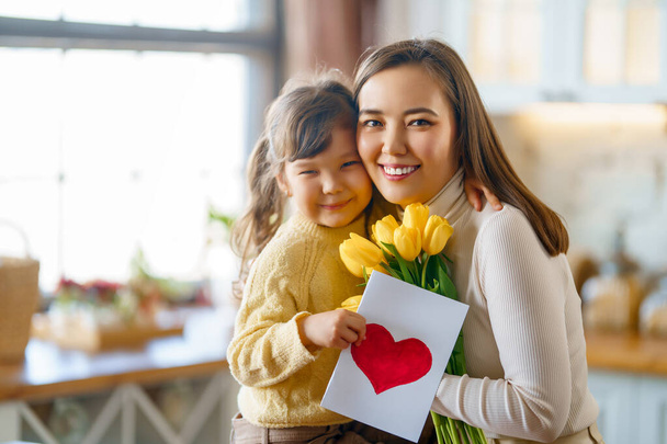 Happy mother's day. Child daughter congratulating her mother and giving her postcard and bouquet of flowers. - Φωτογραφία, εικόνα
