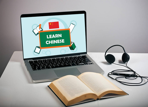 Laptop képernyőn jelenik meg tanulni kínai poszter és egy könyv headset fehér asztal. szürke háttérrel elszigetelve. szelektív fókuszkép. - Fotó, kép