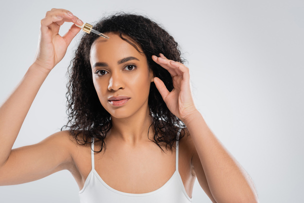 pretty african american woman with perfect skin applying cosmetic serum isolated on grey - Fotoğraf, Görsel