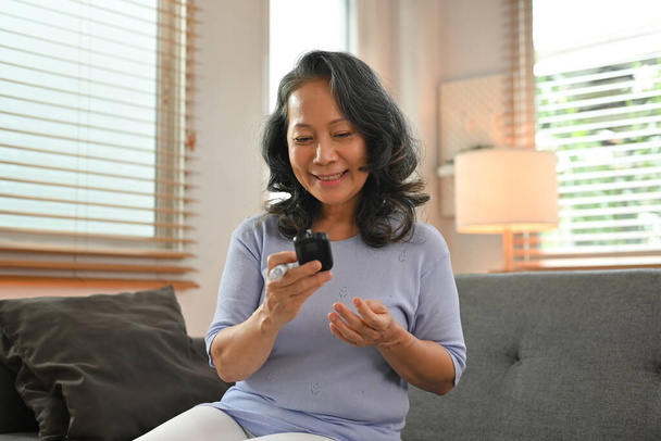 Happy senior woman checking blood sugar level by digital glucose meter. Healthcare and medical, diabetes concept. - Photo, image