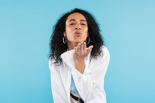 brunette african american woman blowing air kiss and looking at camera isolated on blue - Zdjęcie, obraz