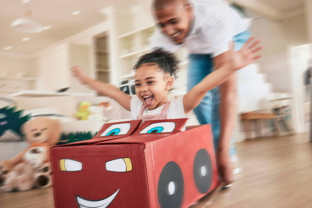 Playing girl, father and box in living room for pushing, games or race in motion blur, bonding love or happiness. Man, female child or cardboard car for support, fast game and floor in family home. - Photo, Image