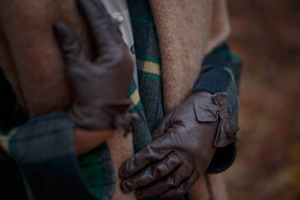 Жіночі руки в коричневих шкіряних рукавичках на тлі теракотового вовняного шарфа і плетеного пальто
 - Фото, зображення