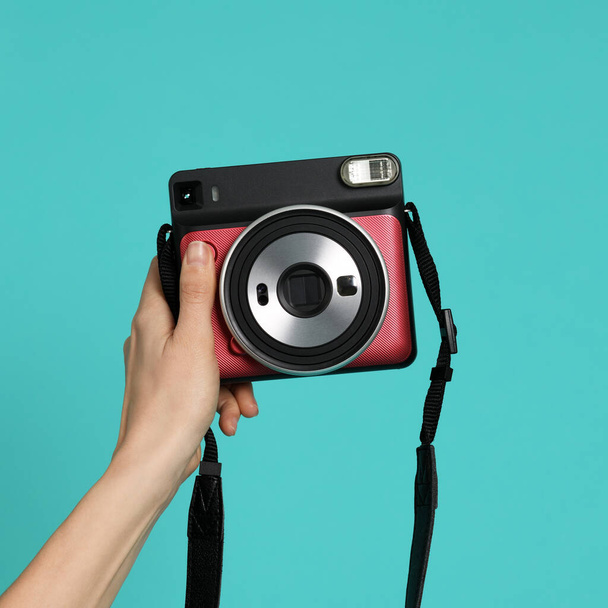 Hand with instant camera on mint background - Zdjęcie, obraz