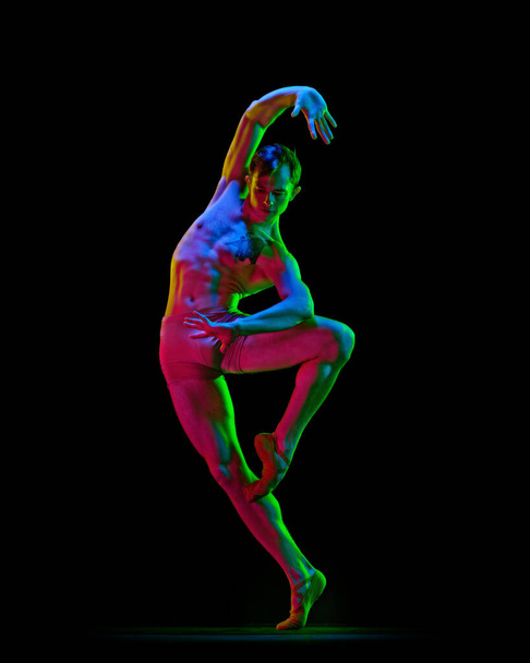 Portrait of young handsome, muscle men, ballet dancer in pastel color clothes posing over dark background with neon light. Contemporary dance style. Concept of classic dance, artist, beauty - Fotografie, Obrázek